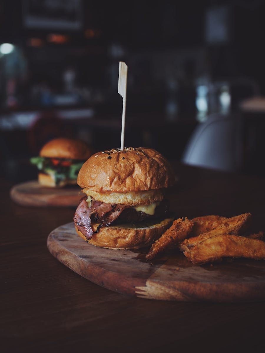 Delicious gourmet beef burger served with crispy sweet potato fries on a rustic wooden board.