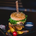 Close-up of a gourmet cheeseburger with wedges and tomato on a black plate.