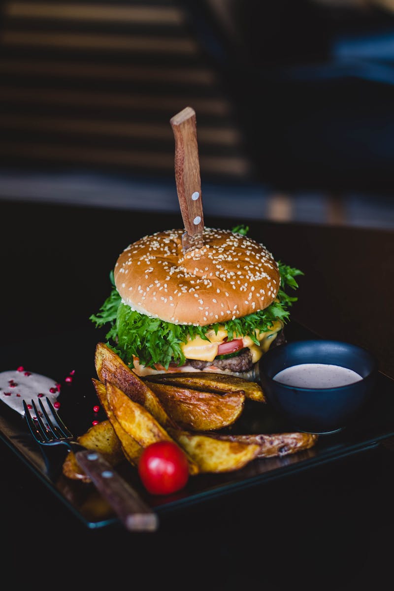 Close-up of a gourmet cheeseburger with wedges and tomato on a black plate.