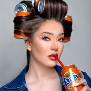 Portrait of a fashionable woman with soda can hair rollers sipping a drink.