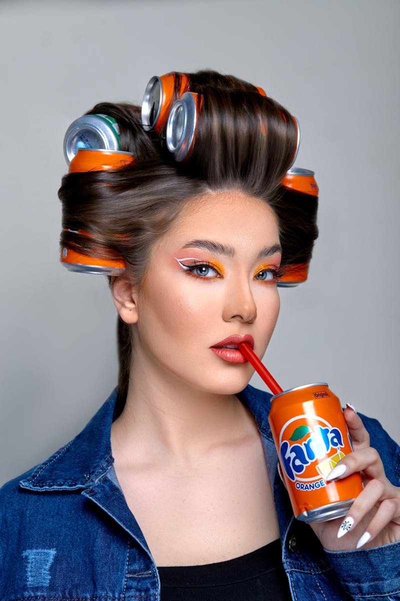 Portrait of a fashionable woman with soda can hair rollers sipping a drink.