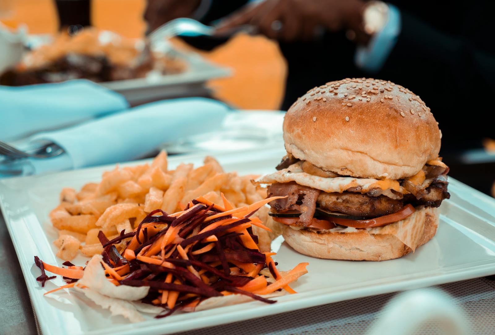 Close-up of a gourmet burger with fries and colorful coleslaw on a white plate, perfect for lunch or dinner.