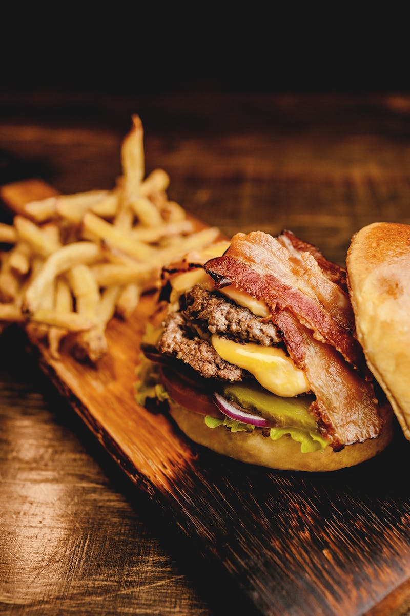 Savor a mouthwatering bacon cheeseburger with crispy fries on a rustic wooden board. Perfect fast food indulgence.