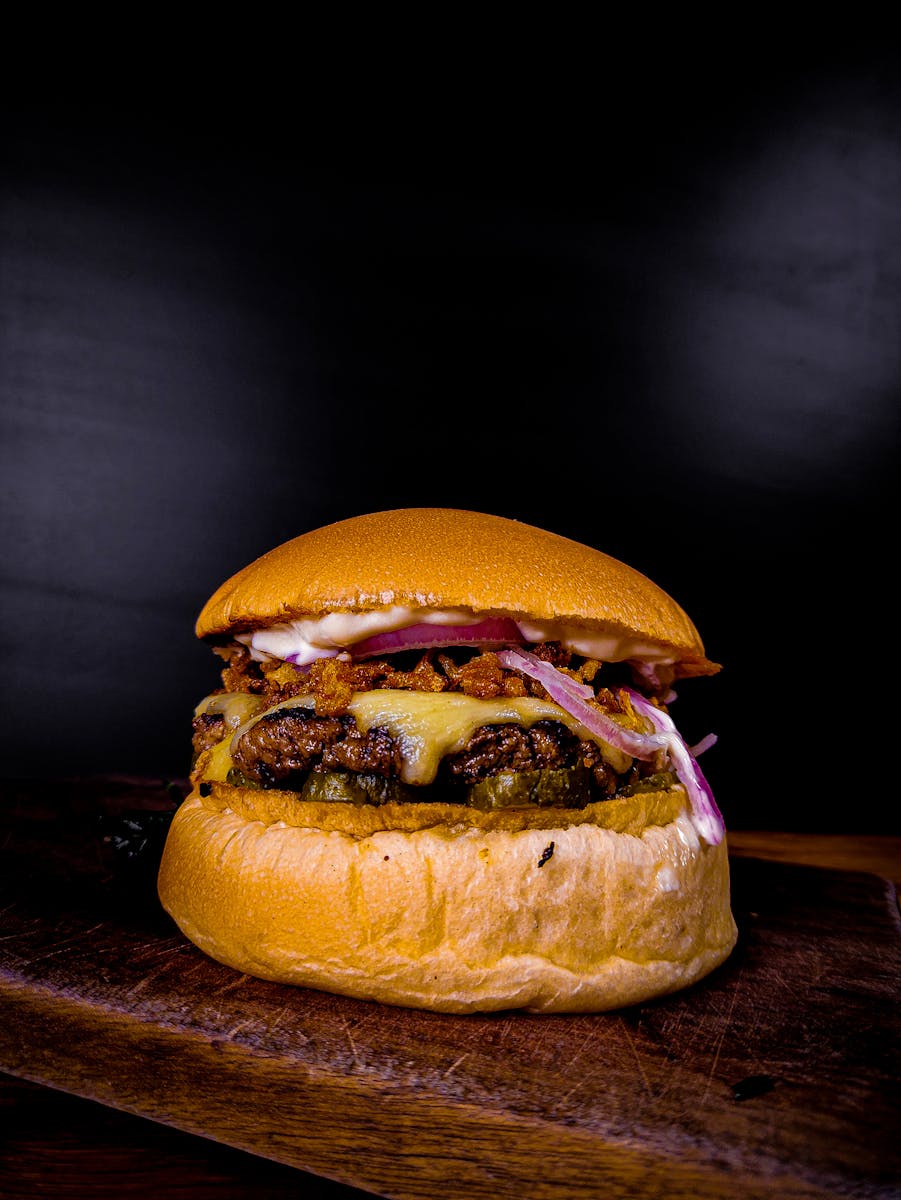 Delicious cheeseburger with melted cheese, onions, and sauce on a wooden board against a dark background.