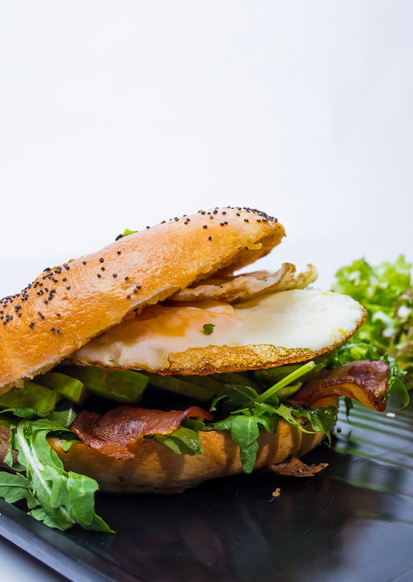 Tasty bagel sandwich with egg, bacon, and greens on a plate, perfect breakfast choice.