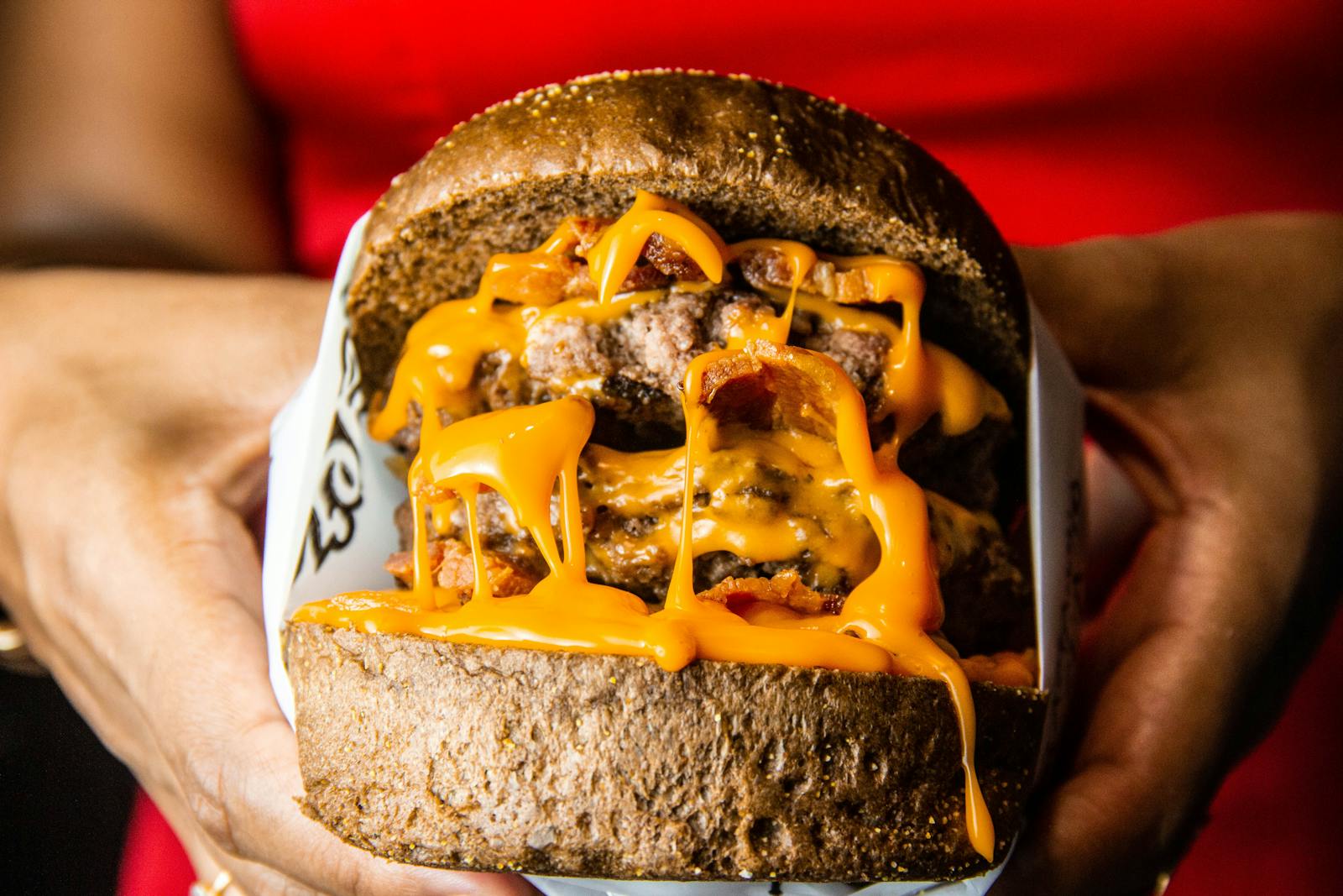 Close-up of a juicy cheeseburger with bacon and melted cheese in hands, perfect for fast food lovers.