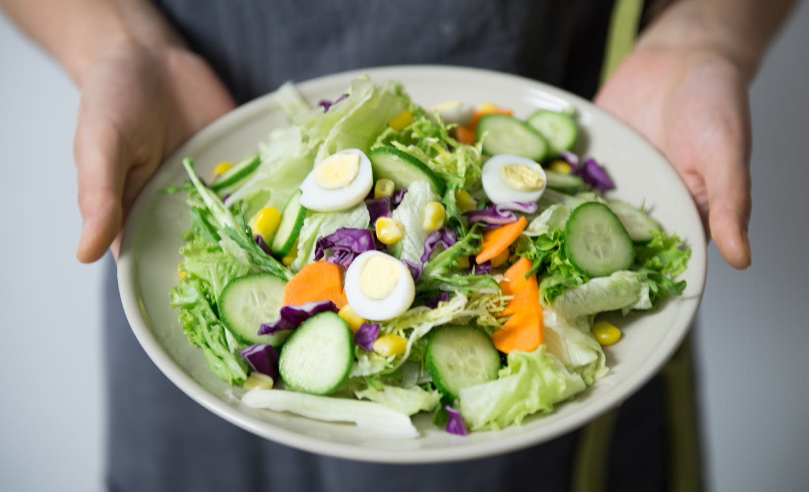 Freshly prepared salad with cucumber, lettuce, carrots, and egg slices presented on a plate.