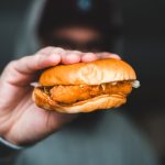 A hand holding a mouth-watering chicken burger, perfect for fast-food lovers.