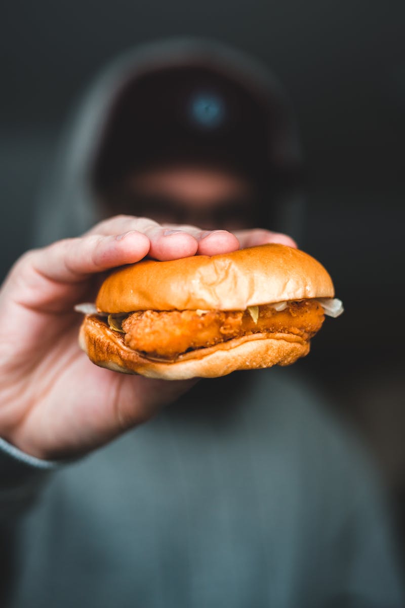 A hand holding a mouth-watering chicken burger, perfect for fast-food lovers.