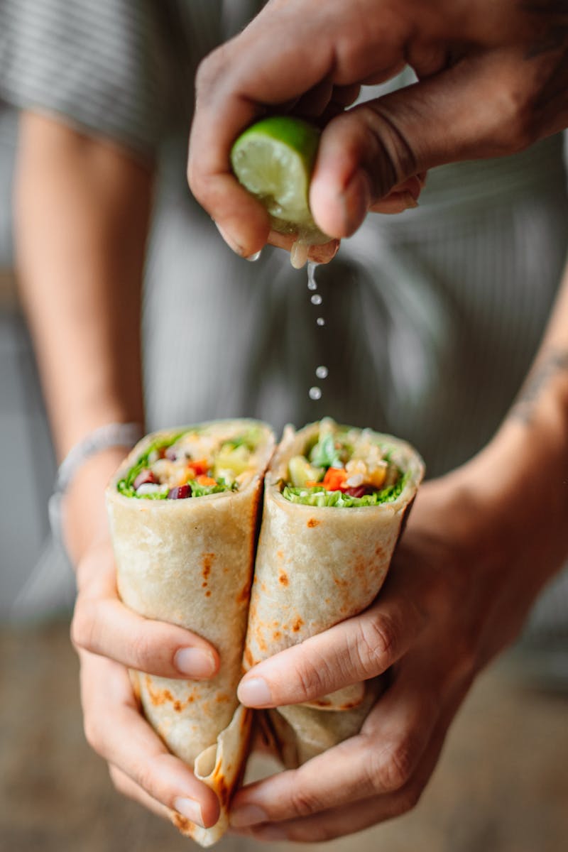 Close-up of hands squeezing lime over delicious vegetable wrap, enhancing its flavor and freshness.