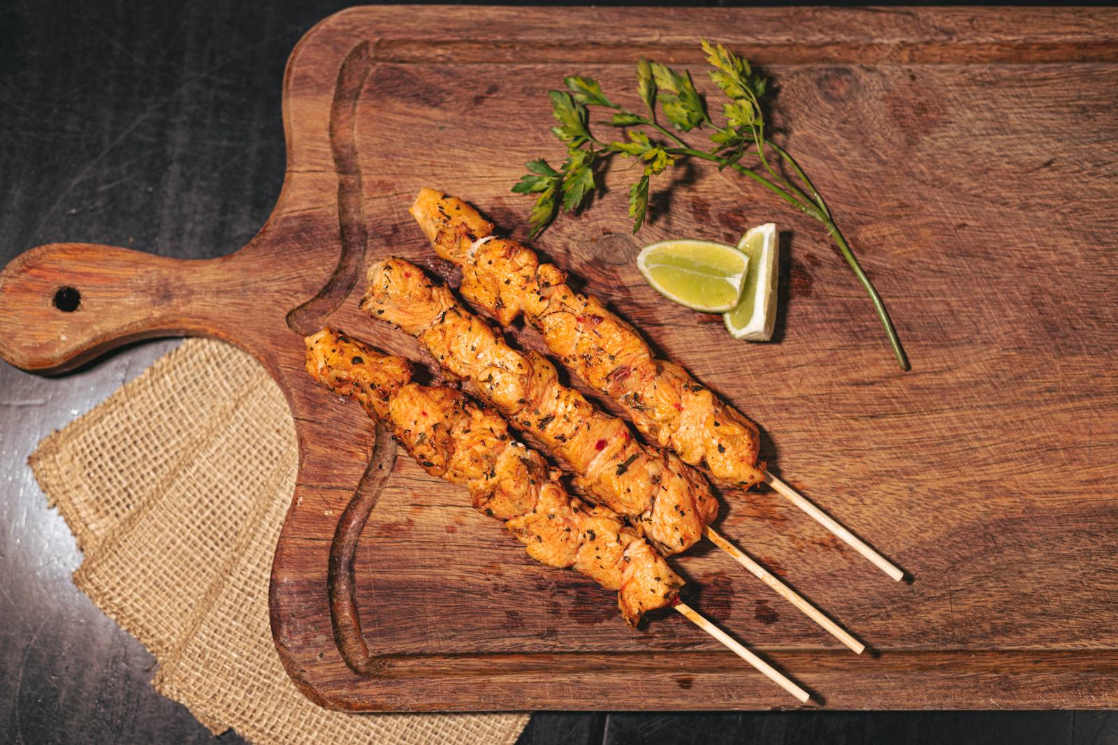 Juicy grilled chicken skewers on a wooden board with lime and herbs.