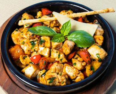 A vibrant grilled chicken salad garnished with fresh basil leaves and served in a rustic bowl.