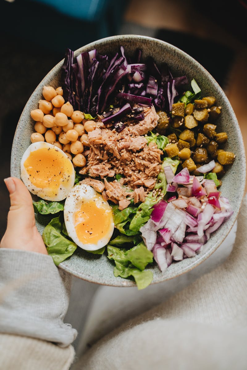 Nutritious bowl featuring tuna, boiled eggs, chickpeas, vegetables, and lettuce for a healthy meal.