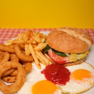 Mouthwatering breakfast plate featuring a burger, crispy fries, fried eggs with ketchup on a vibrant yellow background.