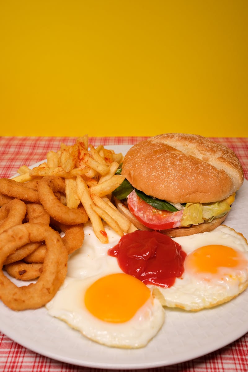 Mouthwatering breakfast plate featuring a burger, crispy fries, fried eggs with ketchup on a vibrant yellow background.