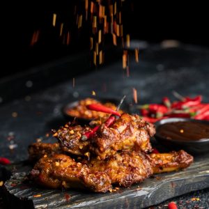 Delicious spicy chicken wings with chilies and spices on dark background.