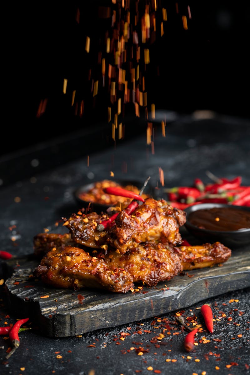 Delicious spicy chicken wings with chilies and spices on dark background.