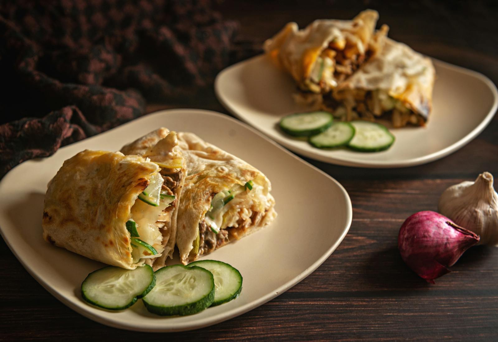 Delicious shawarma wraps garnished with sliced cucumbers on a rustic plate setting.