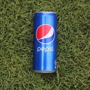 a can of pepsi sitting on top of a lush green field