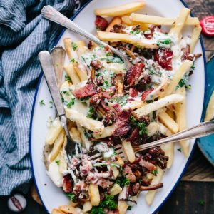 bacon strips and melted cheese topped fries on oval white and blue platter with gray stainless steel forks