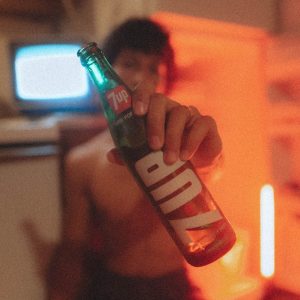 Boy holding a 7up bottle in a vintage kitchen setting with warm lighting.