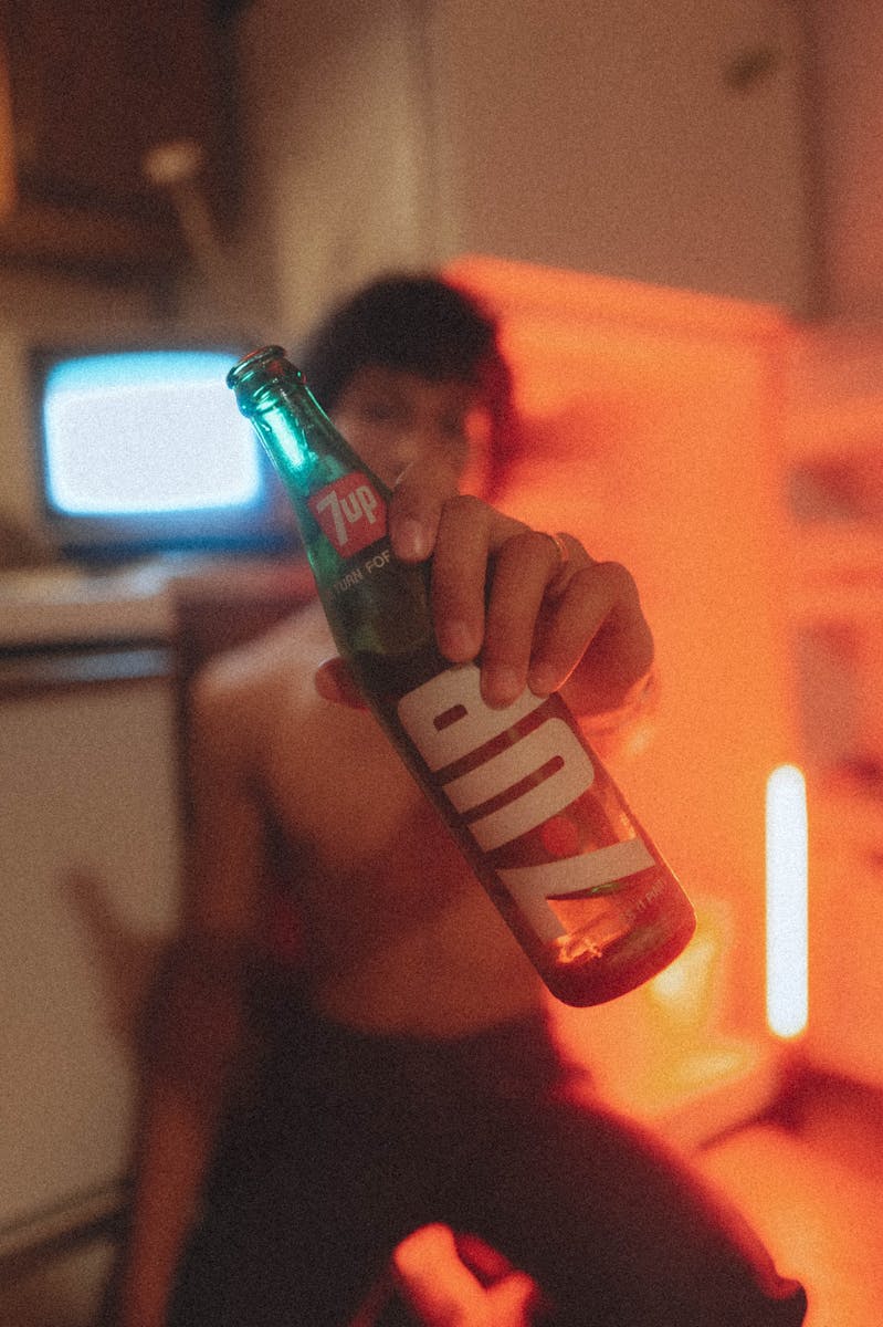 Boy holding a 7up bottle in a vintage kitchen setting with warm lighting.