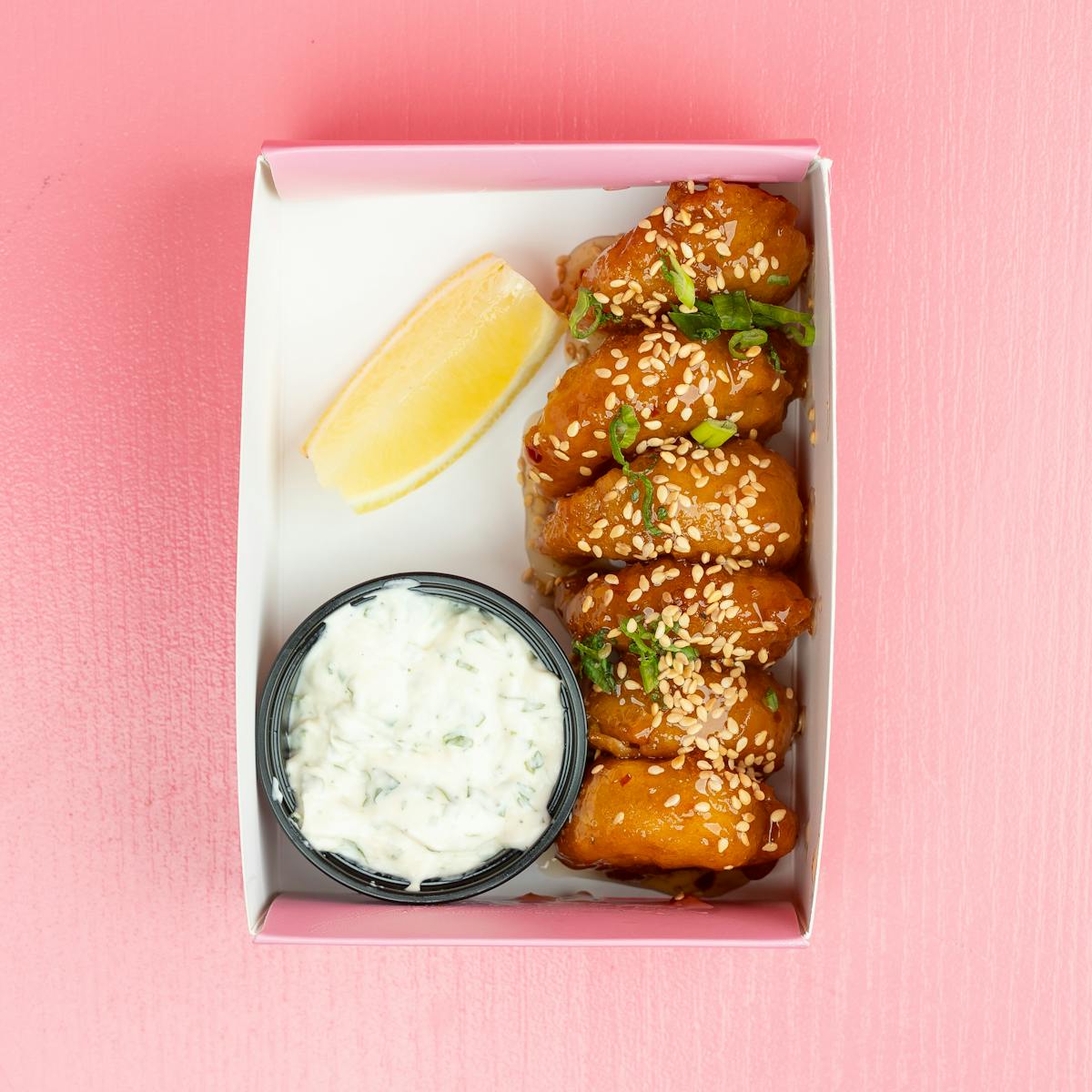 Delicious sesame chicken wings served with dip and lemon wedge in a takeaway box.