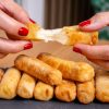 Close-up of hands with red nails pulling apart melted cheese stick, revealing gooey inside.