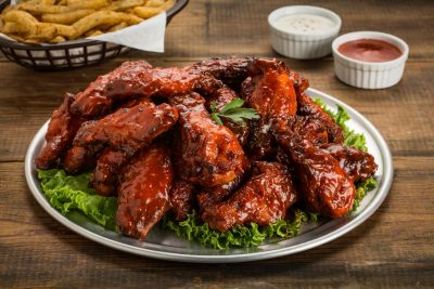 Tasty BBQ chicken wings served with green lettuce and dipping sauces on a wooden table.