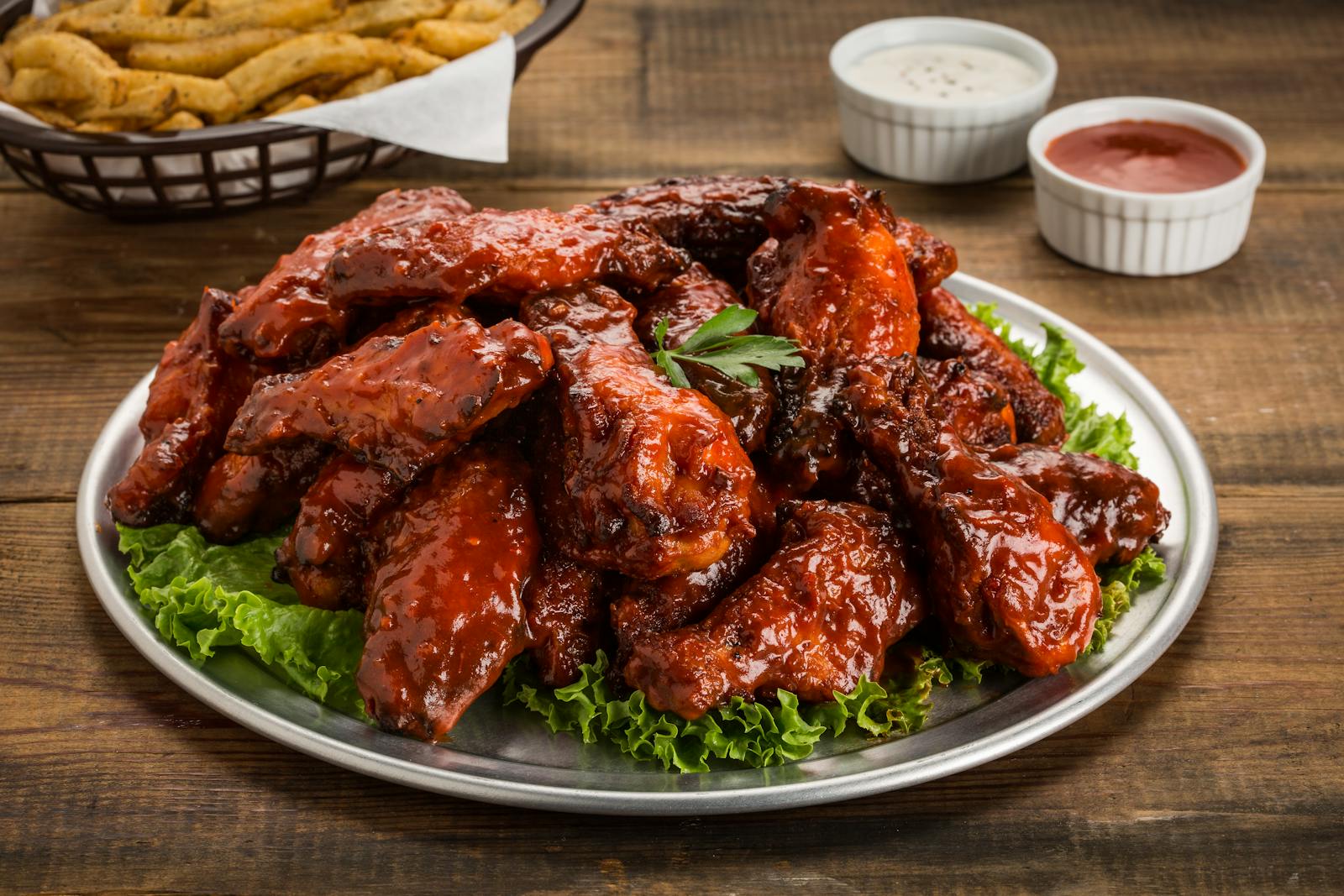 Tasty BBQ chicken wings served with green lettuce and dipping sauces on a wooden table.