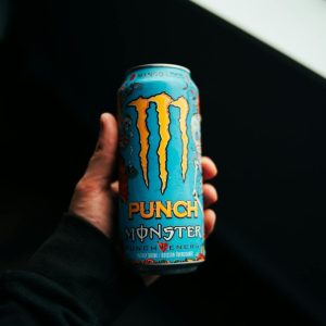 A close-up shot of a hand holding a Monster Punch energy drink can with a dark background.