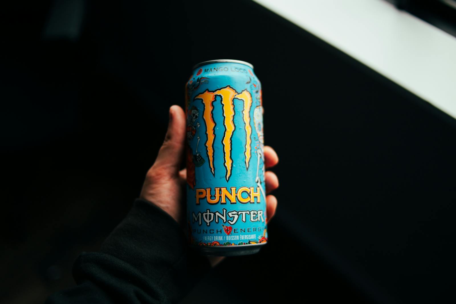 A close-up shot of a hand holding a Monster Punch energy drink can with a dark background.